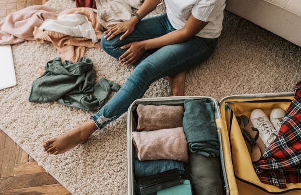 Femme préparant sa valise pour un déménagement, entourée de vêtements et d’effets personnels, en veillant à transporter ses appareils avec batteries au lithium en toute sécurité.