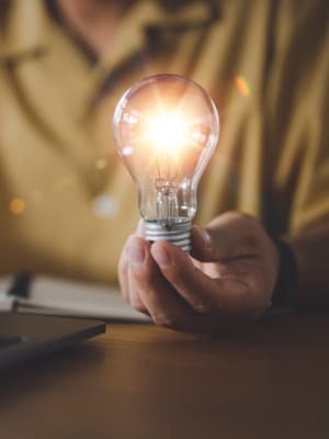 Main tenant une ampoule, illustrant les conseils et guides pratiques de Grospiron